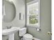 Powder room features a pedestal sink, round mirror, and a window offering natural light at 67 Camden Circle, Pawleys Island, SC 29585