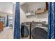 Modern laundry room with side-by-side washer and dryer units, convenient shelving, and stylish blue curtain at 1209 Eagle Creek Dr., Myrtle Beach, SC 29588