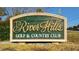 Eye-level view of the River Hills Golf & Country Club sign with green background and gold lettering at 3334 Cedar Creek Run, Little River, SC 29566