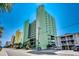 Street view of a multi-story condo building with balconies, palm trees, and ample parking at 5310 N Ocean Blvd. # 10B, North Myrtle Beach, SC 29582