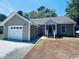 Tan single story home featuring an attached garage, gray roof, manicured lawn and welcoming front porch at 1000 Weldon Ln., Conway, SC 29526