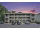 Three-story condominium building with multiple decks and parking spaces, set against a vibrant sunset sky at 1460 Blue Tree Ct. # E, Myrtle Beach, SC 29588