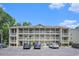 Three-story condo building with multiple balconies, parking spaces, and lush landscaping on a sunny day at 1460 Blue Tree Ct. # E, Myrtle Beach, SC 29588