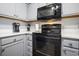 Close-up of kitchen appliances, including a black microwave and stove above gray cabinets at 310 Marsh Pl. # 108, Murrells Inlet, SC 29576