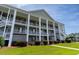 Three-story condo building featuring elevated decks, white columns, and lush landscaping at 5852 Longwood Dr. # 302, Murrells Inlet, SC 29576