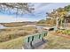 Picturesque marsh view with a green bench in the foreground, a dock, and a building under a clear sky at 135 S Dunes Dr. # 501, Pawleys Island, SC 29585