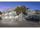Three-story condominium building featuring stairwells and multiple balconies, surrounded by trees and ample parking spaces at 300 47Th Ave. S # 1F, North Myrtle Beach, SC 29582