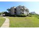 Multi-story condo building with balconies, green lawn, and palm trees under a clear blue sky at 1582 South Waccamaw Dr. # 56, Garden City Beach, SC 29576