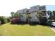Multi-story condo building with green lawn, shrubbery, and palm trees under a clear blue sky at 1582 South Waccamaw Dr. # 56, Garden City Beach, SC 29576