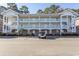 Three-story condo building with exterior stairs, white railings, and ample parking in a landscaped community at 690 Riverwalk Dr. # 201, Myrtle Beach, SC 29579