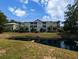 Condo exterior with a pond view, lush landscaping, balconies, and green siding under a blue sky at 82 Mingo Dr. # 2D, Pawleys Island, SC 29585