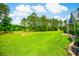 Lush green backyard featuring a spacious lawn, mature trees, and a white bench seating area at 1013 Happy Ln., Galivants Ferry, SC 29544