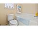 A bathroom featuring a soaking tub with a blue bath mat, a toilet and a window with decorative items at 1222 Midtown Village Dr., Conway, SC 29526