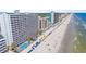 Expansive aerial view of resort buildings, sandy beach, ocean waves, and blue and yellow umbrellas on the beach at 1012 N Waccamaw Dr. # 1107, Murrells Inlet, SC 29576