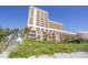 Exterior view of a tall condo building from the beach. Lush vegetation in the foreground at 6900 N Ocean Blvd. # 840, Myrtle Beach, SC 29572