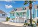 Charming two-story turquoise beach home with white trim, a balcony, and a lush palm tree in the front at 4534 Landing Rd., Little River, SC 29566