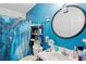 Bright bathroom with blue walls, a round mirror, a shelf rack and a shower with a decorative blue curtain at 10071 Kings Rd., Myrtle Beach, SC 29572