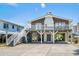 Exterior view of elevated beach home with white railings, gray stairs and brick facade at 204 55Th Ave. N, North Myrtle Beach, SC 29582