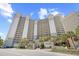 Exterior view of a high-rise condo building with palm trees and a clear blue sky at 4800 S Ocean Blvd. # 514, North Myrtle Beach, SC 29582