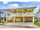 Charming yellow stilted beach house with a covered parking area and a cozy balcony with ceiling fans at 121 Easy St., Garden City Beach, SC 29576