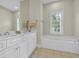 Bright bathroom featuring a double vanity, a large mirror, and a soaking tub near a window with plantation shutters at 179 Cottage Ct., Pawleys Island, SC 29585