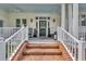 Warm, welcoming front porch with brick steps, white railings, rocking chairs, and a stylish front door with a wreath at 179 Cottage Ct., Pawleys Island, SC 29585