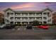 Three story condominium building with white railings, green siding, and ample parking spaces at dusk at 3951 Gladiola Ct. # 104, Myrtle Beach, SC 29588