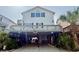 Two story beach home with a sign, white siding, and covered parking with a golf cart underneath at 6001-B5 S Kings Hwy., Myrtle Beach, SC 29575
