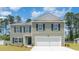 Charming two-story home featuring a two-car garage, gray siding, and green shutters against a backdrop of trees and a blue sky at 743 Chazen Way, Longs, SC 29568