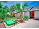 Landscaped front yard with a putting green and mature palm trees, leading to a home with a vibrant red front door at 10056 Kings Rd., Myrtle Beach, SC 29572