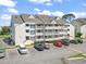 Three-story condo building with ample parking and balconies against a blue sky with fluffy white clouds at 1100 Possum Trot Rd. # F218, North Myrtle Beach, SC 29582