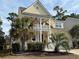 Charming yellow two-story home featuring double porches, an American flag, and lush tropical landscaping at 821 Falkirk St., Myrtle Beach, SC 29579