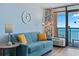 Living room with a turquoise sofa, round clock, lamp, and ocean view balcony at 1501 S Ocean Blvd. # 1039, Myrtle Beach, SC 29577