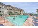 Community pool featuring people swimming, lounge chairs, and the exterior of the condo complex with palm trees at 5601 N Ocean Blvd. # E-113, Myrtle Beach, SC 29577