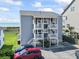 Three story condo building with white railings and stairs with a parking lot and partial ocean view at 4105 S Ocean Blvd. # 102, North Myrtle Beach, SC 29582