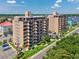 Condo building with a beige facade, balconies, green lawn, mature trees, and parking spaces on a sunny day at 7601 N Ocean Blvd. # 3-B, Myrtle Beach, SC 29572