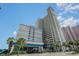 Exterior view of high-rise condo building entrance featuring elegant portico, lush landscaping, and adjacent palm trees at 2504 N Ocean Blvd. # 936, Myrtle Beach, SC 29577