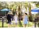 Three women walking on outdoor tennis courts with blue umbrellas and palm trees on a sunny day at 223 Atlantic Breeze St., Myrtle Beach, SC 29572