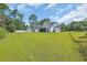 Green backyard view of a white modern home with dark roof and large green grass and scattered trees at 2192 Eastwoods Dr., Conway, SC 29526