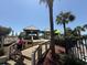 View of a wooden walkway with a small pool bar and people with palm trees and a blue sky at 4800 S Ocean Blvd. # 706, North Myrtle Beach, SC 29582