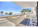 Balcony view overlooking the beach, showcasing the ocean, palm trees, and outdoor seating at 101 Ocean Creek Dr. # Jj-1, Myrtle Beach, SC 29572