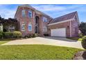 A two-story brick house showcasing a three-car garage and a beautifully landscaped yard at 6575 Sw Longwater Ct., Ocean Isle Beach, NC 28469