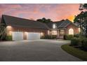 Well-lit brick home boasts an oversized three-car garage and a spacious driveway at sunset at 598 Summer Green Ct., Sunset Beach, NC 28468