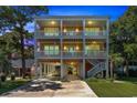 Gorgeous three-story beach house with illuminated balconies and covered parking, showcasing its elegance at twilight at 3304 Palm St., North Myrtle Beach, SC 29582