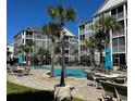 Inviting community pool area with tables, chairs, umbrellas, and multiple palm trees at 181 Ella Kinley Circle # 305, Myrtle Beach, NY 29588