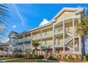 Spacious yellow condominium featuring multiple levels, white railings, a well manicured lawn, and mature palm trees at 4173 Hibiscus Dr. # 204, Little River, SC 29566