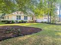 Landscaped front yard of a yellow one-story home featuring mature trees and a lush lawn at 1043 Yellow Jasmine Dr., Longs, SC 29568