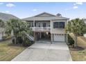 Charming raised beach house featuring a spacious driveway, palm trees and a cozy covered porch and an under-house entertainment area at 619 10Th Ave. S, North Myrtle Beach, SC 29582