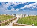 Picturesque beach access with a wooden walkway through lush dunes under a partly cloudy blue sky at 111 Maddux Ln. # B, Myrtle Beach, SC 29588