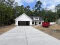 New single-story home with white siding, stone accents, concrete driveway, and a forest backdrop at 1274 Pinetucky Dr., Galivants Ferry, SC 29544